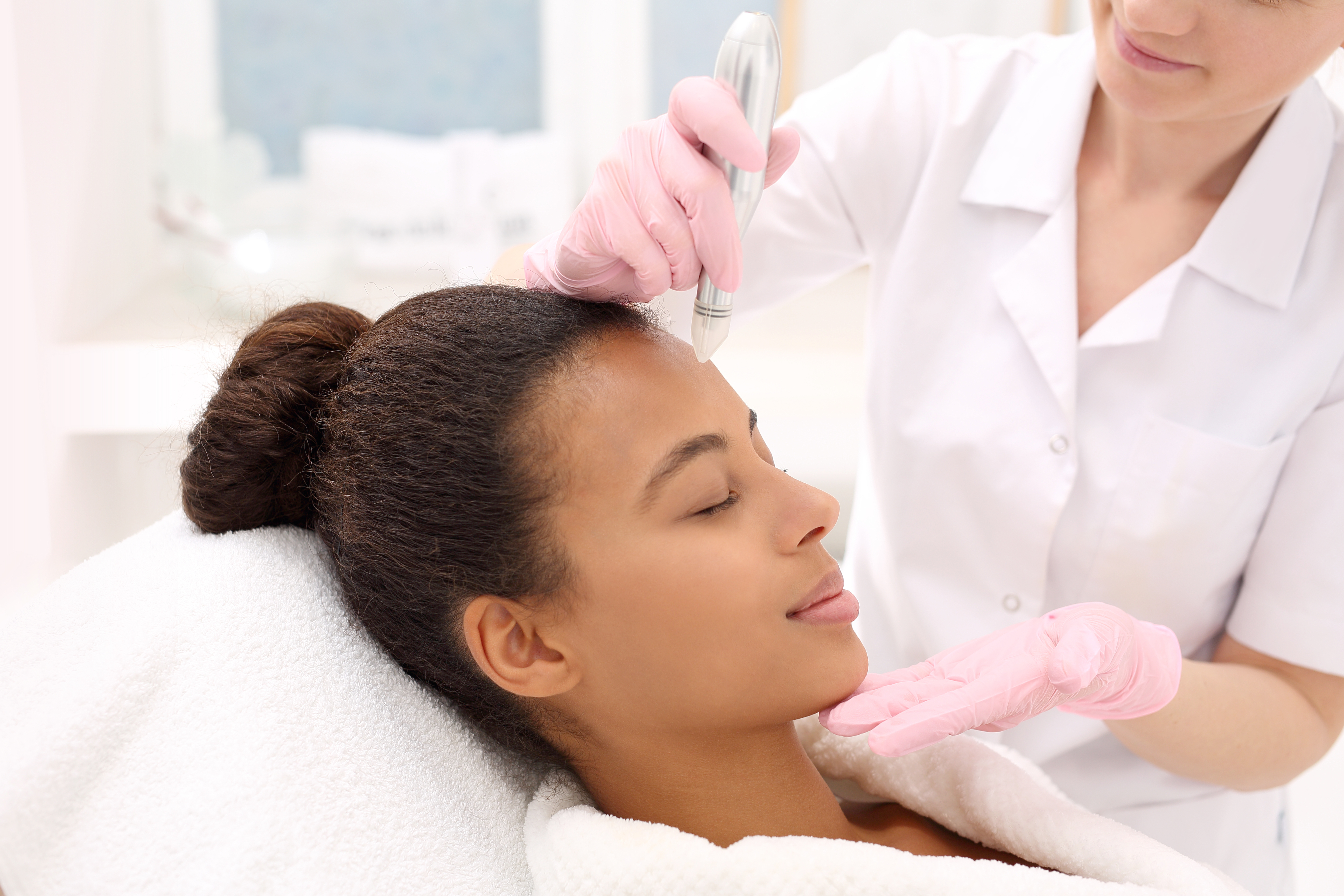 Beautician performs mesotherapy microneedle treatment on a woman's face